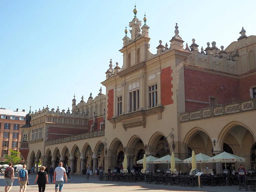 The Cloth Hall in Krakow's Main Market Square with tourists and cafe umbrellas.