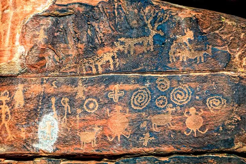 Ancient petroglyphs on reddish rock depicting animal and humanoid figures.